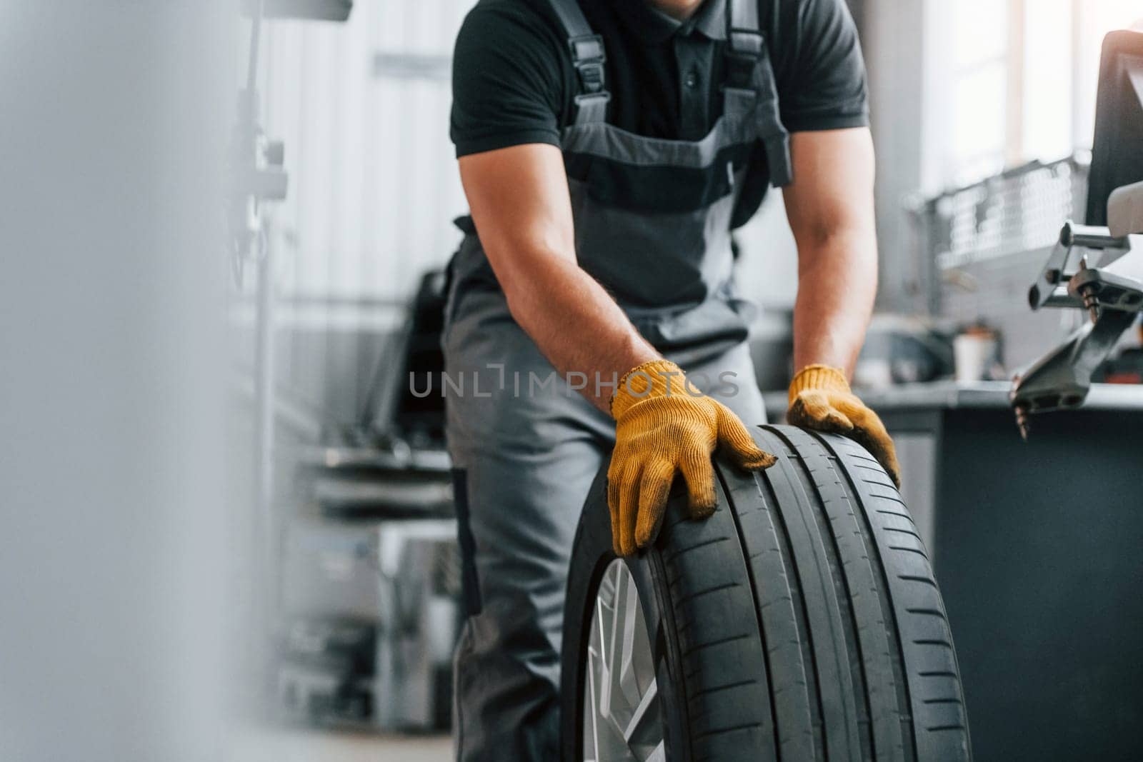 Close up view of wheel. Man in uniform is working in the auto service.