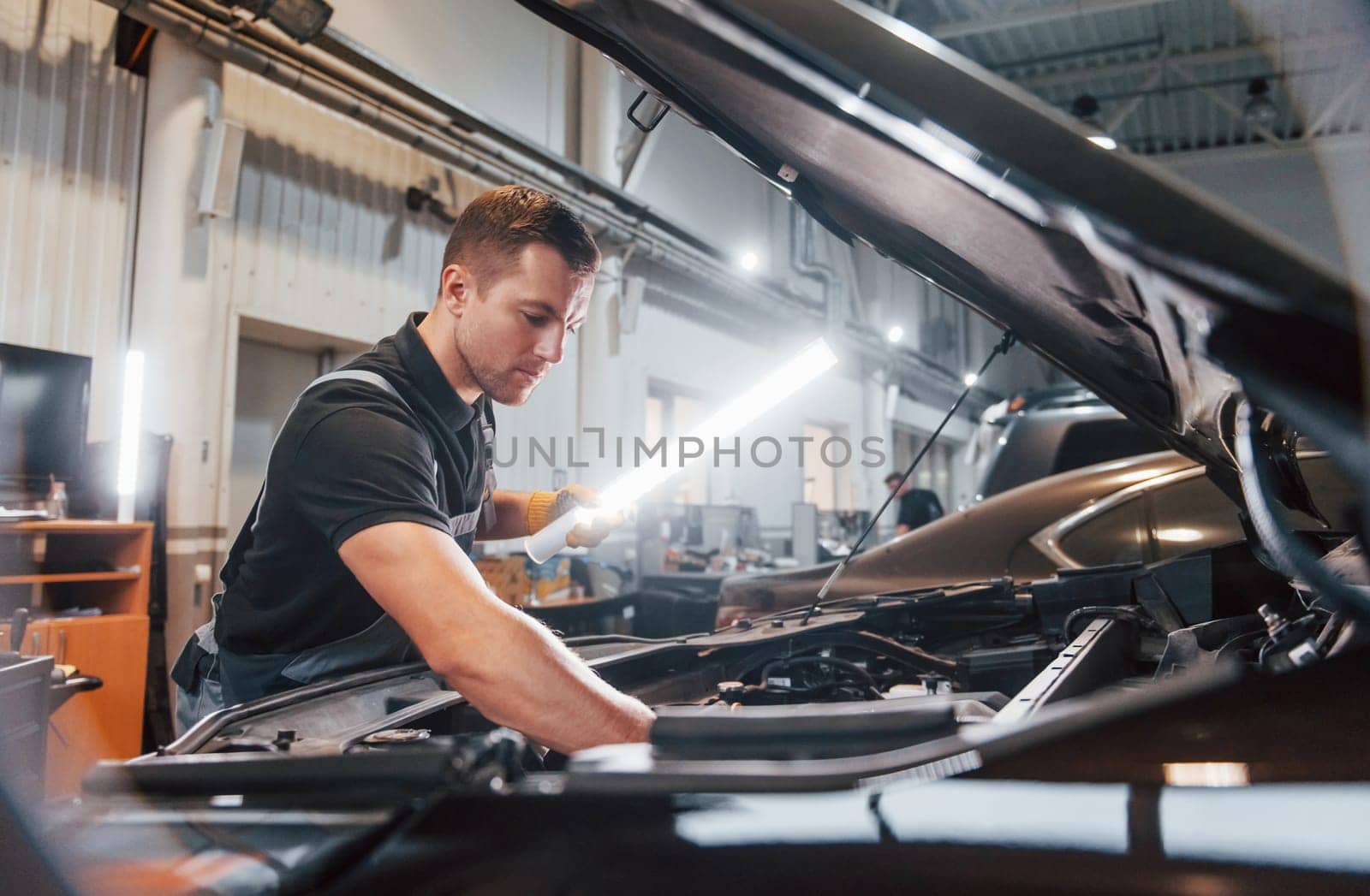 Under the hood. Man in uniform is working in the auto service by Standret