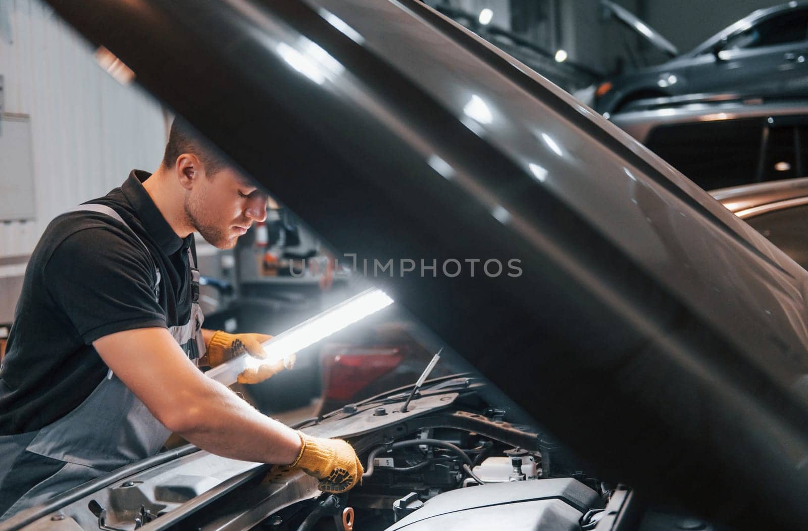 Under the hood. Man in uniform is working in the auto service.