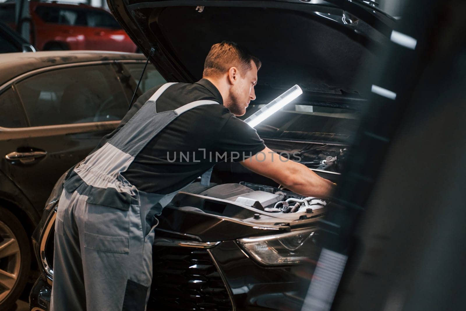 With lighting equipment. Man in uniform is working in the auto service.