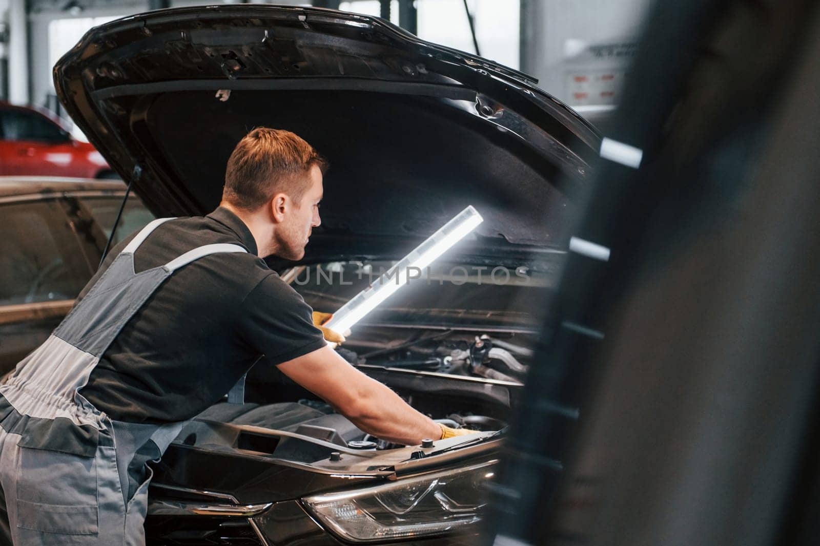 With lighting equipment. Man in uniform is working in the auto service by Standret