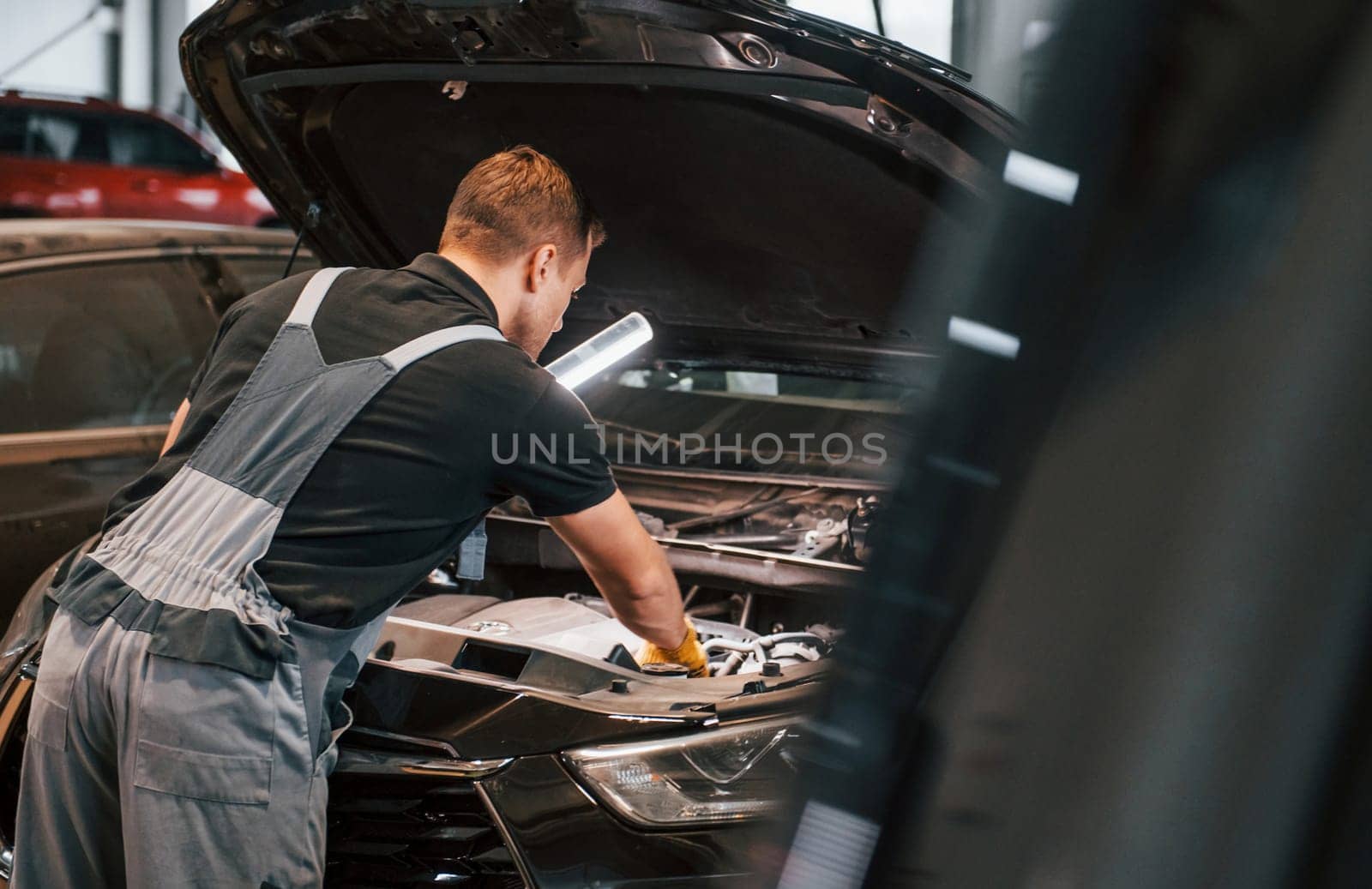 With lighting equipment. Man in uniform is working in the auto service.