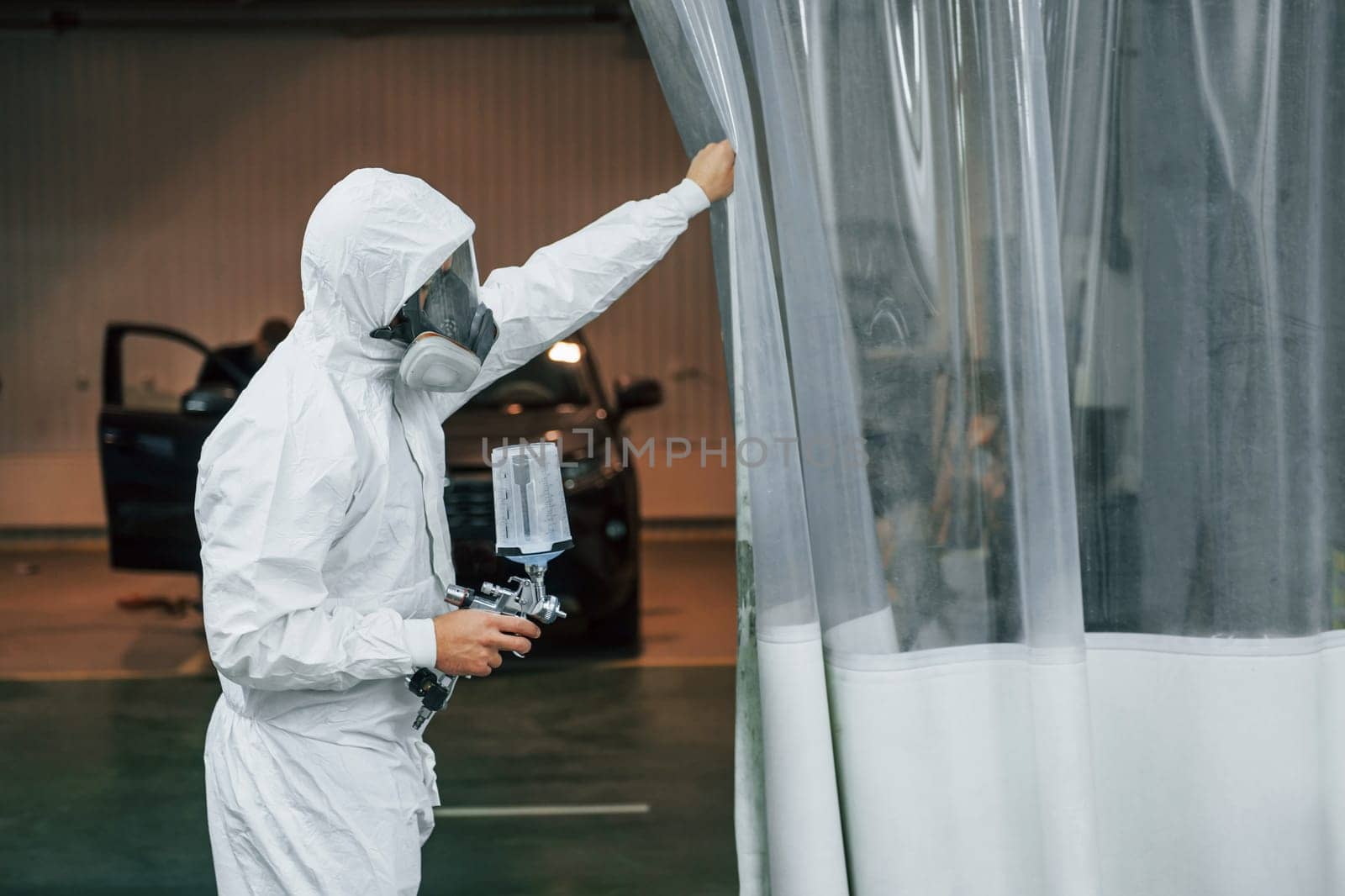 In protective white uniform. Man is working in the auto service.