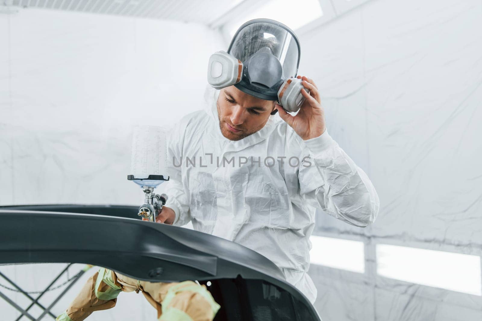 Painting the car. Man in uniform is working in the auto service.
