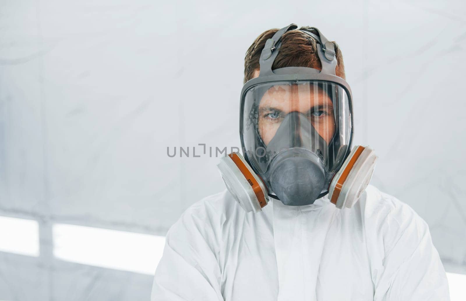 Portrait of man in the protective mask. Worker in uniform is in the auto service.