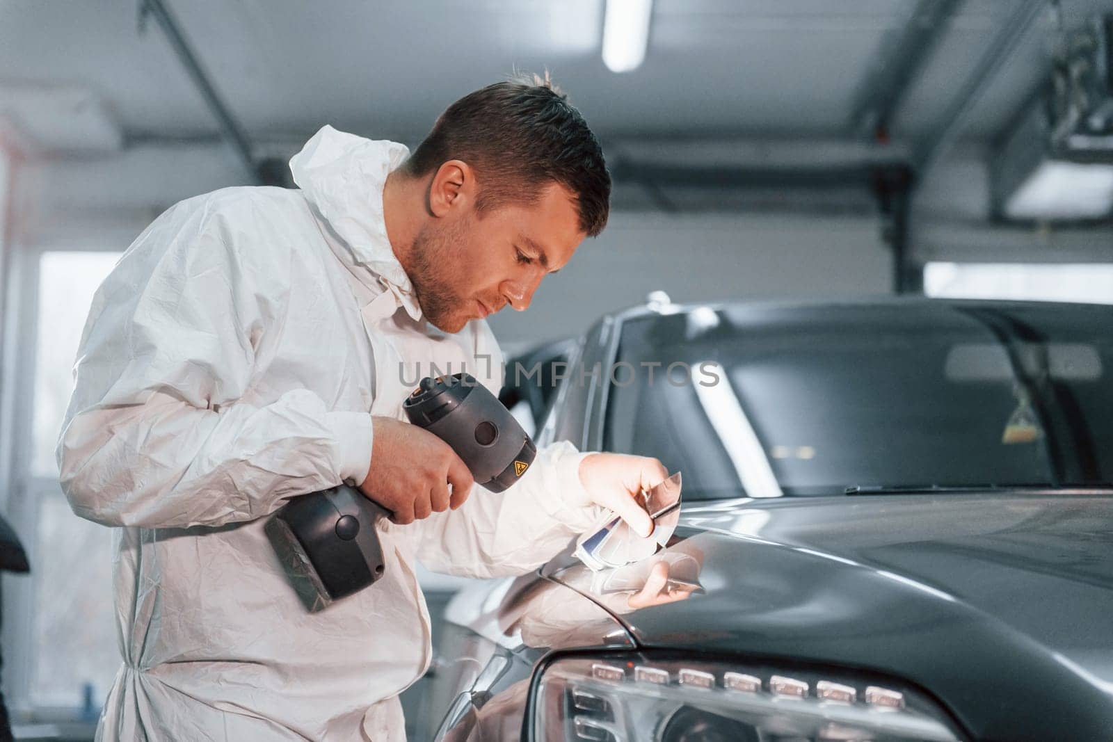 Using special equipment. Man in uniform is working in the auto service.