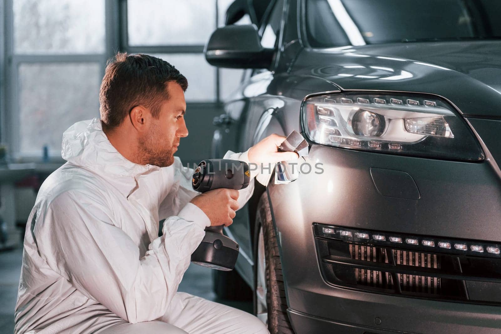 Using special equipment. Man in uniform is working in the auto service by Standret