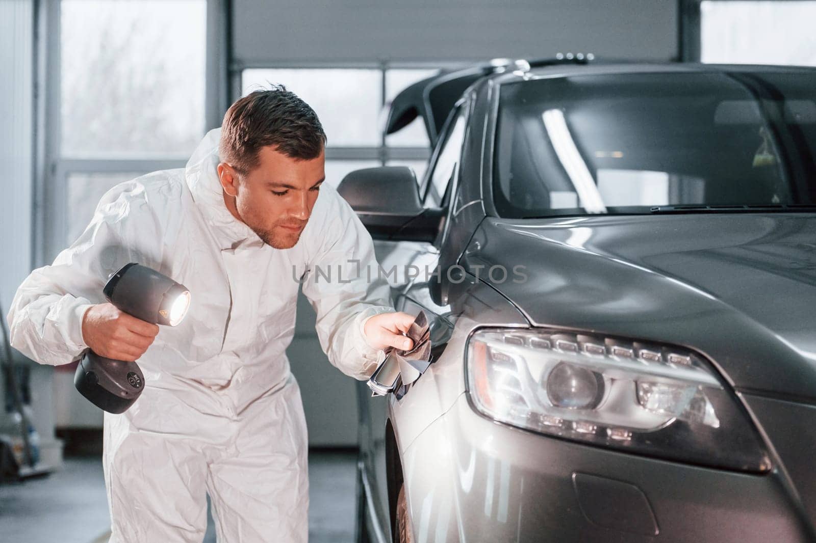 Using special equipment. Man in uniform is working in the auto service by Standret