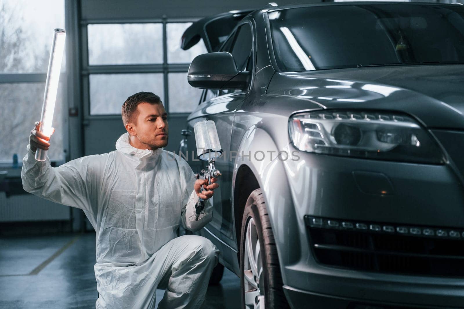 Illuminating the car surface. Man in uniform is working in the auto service by Standret