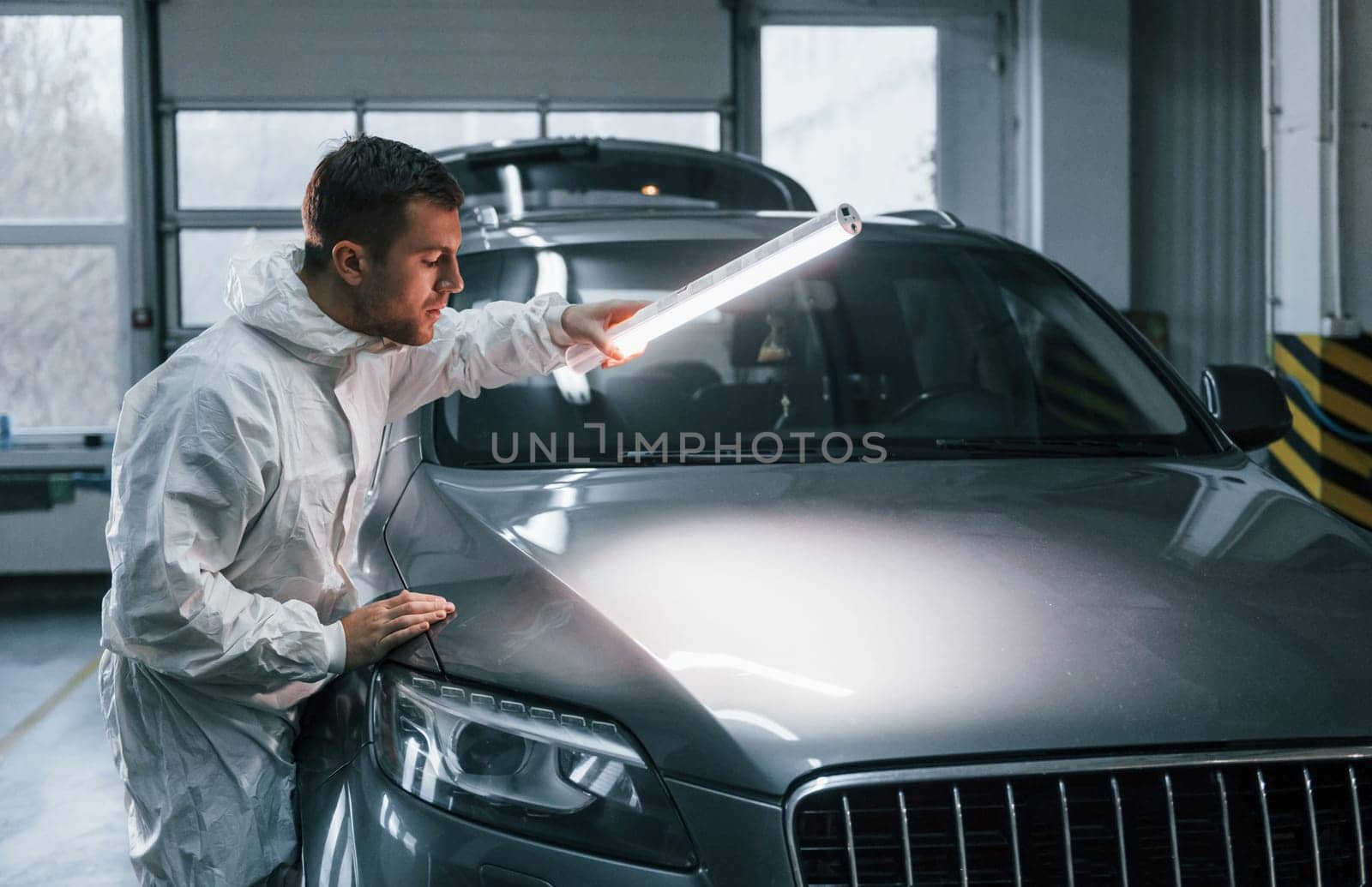 Illuminating the car surface. Man in uniform is working in the auto service by Standret