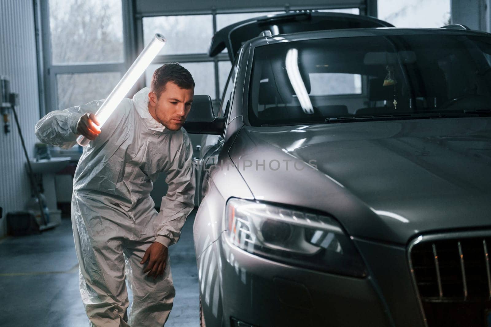 Illuminating the car surface. Man in uniform is working in the auto service by Standret