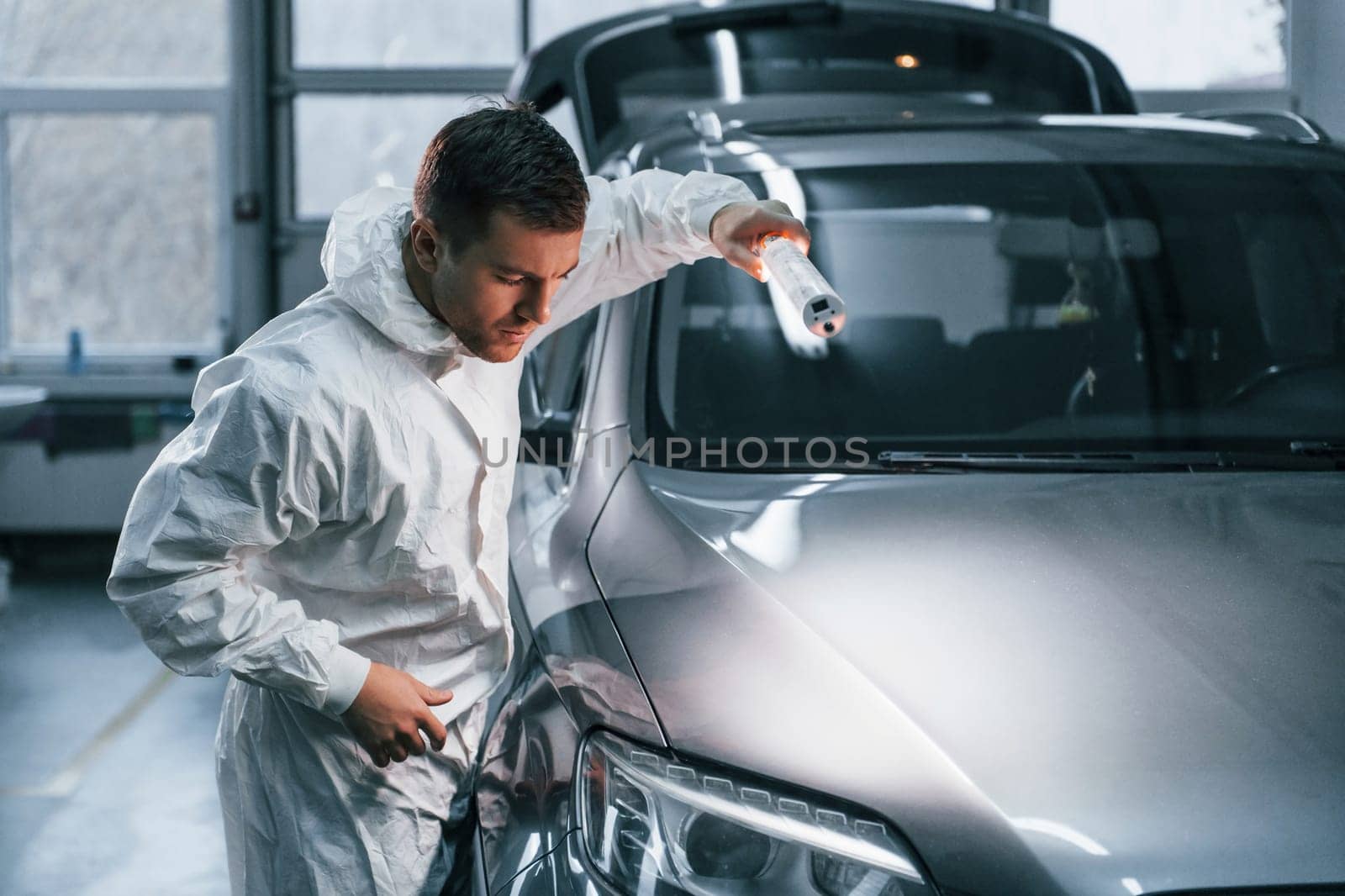 Silver colored car. Man in uniform is working in the auto service.