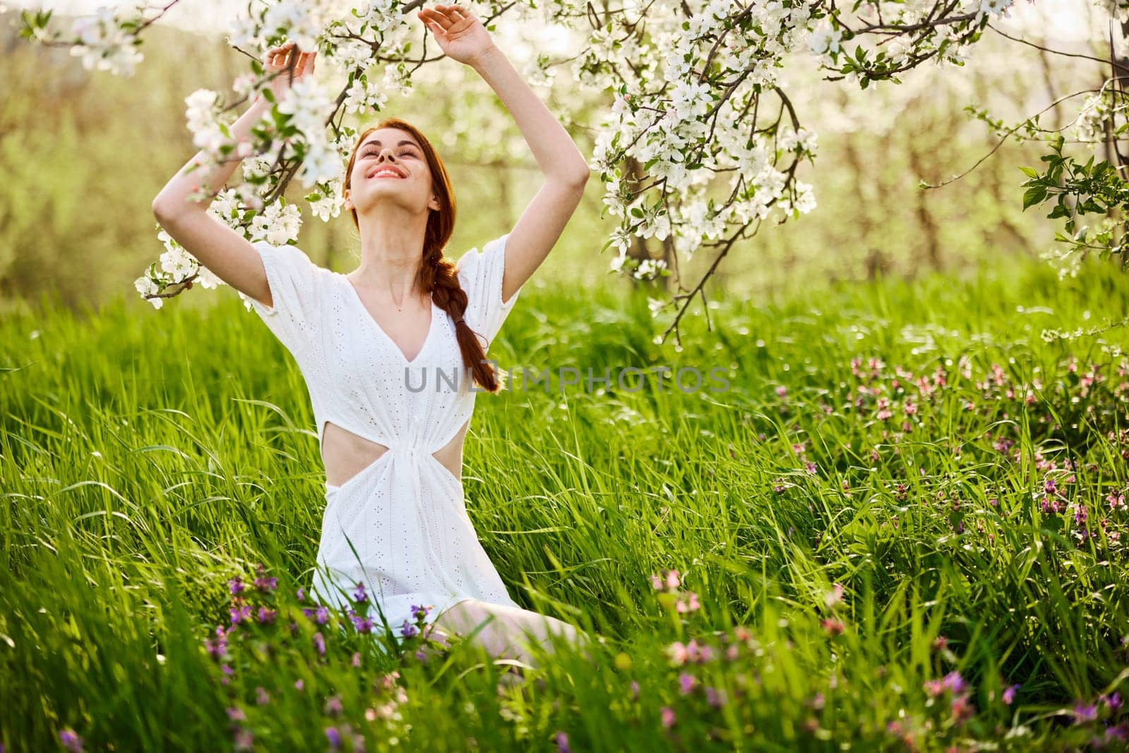 beautiful woman in a light dress posing next to a flowering tree in the countryside by Vichizh