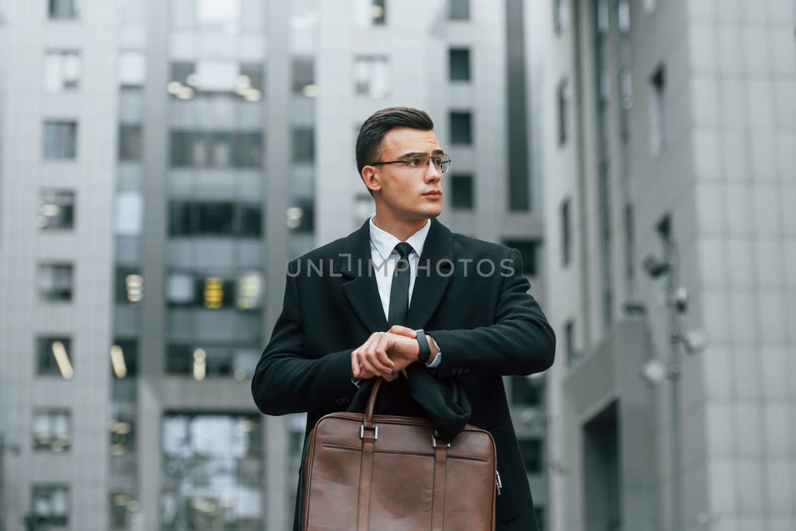 Checking the time. Businessman in black suit and tie is outdoors in the city.