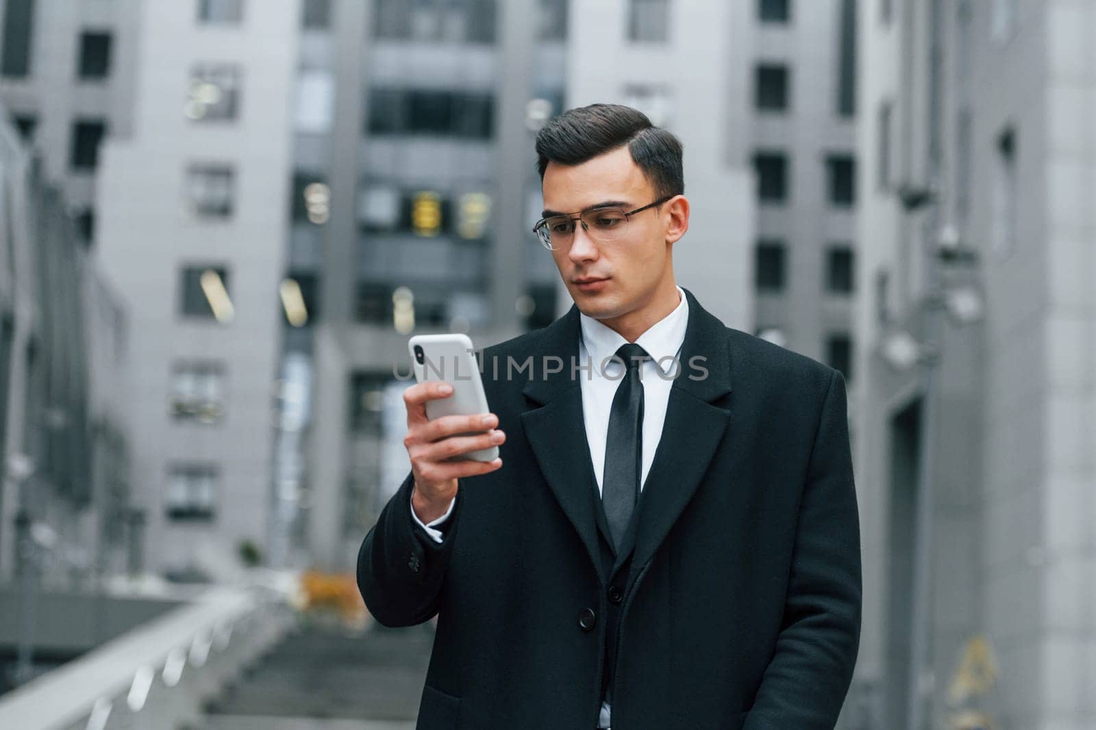 With smartphone. Businessman in black suit and tie is outdoors in the city by Standret