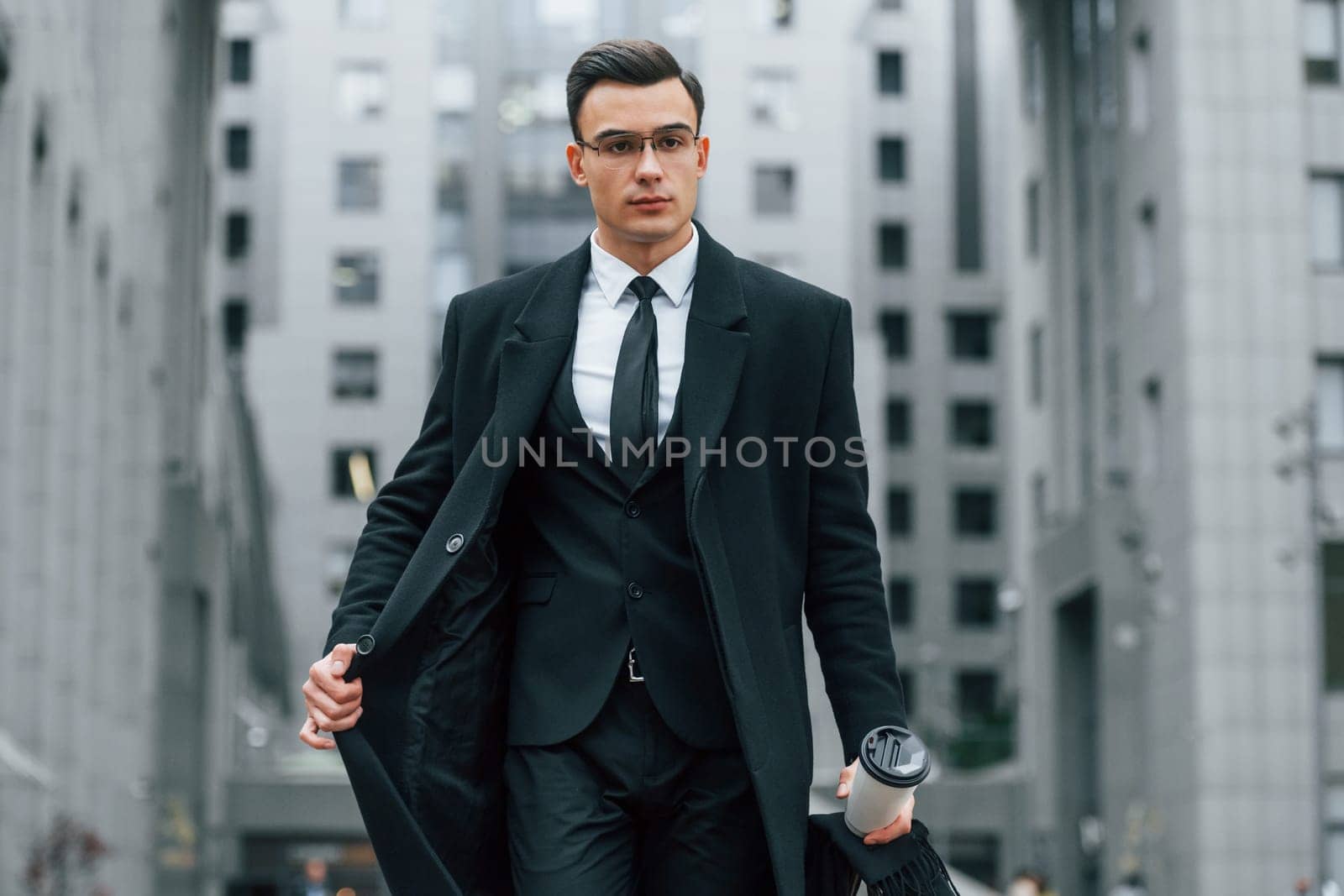 Walking forward. Businessman in black suit and tie is outdoors in the city.