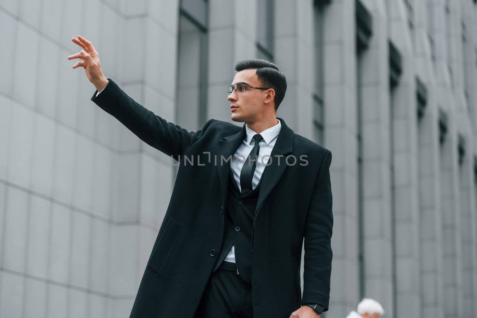 Calling taxi. Businessman in black suit and tie is outdoors in the city.