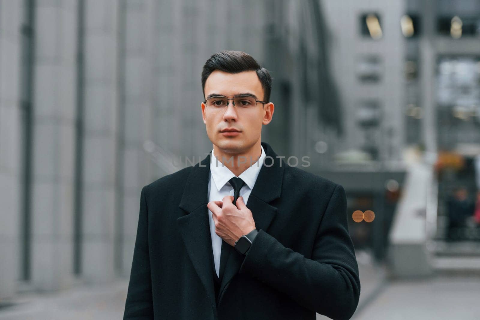 Fixing the tie. Businessman in black suit is outdoors in the city by Standret