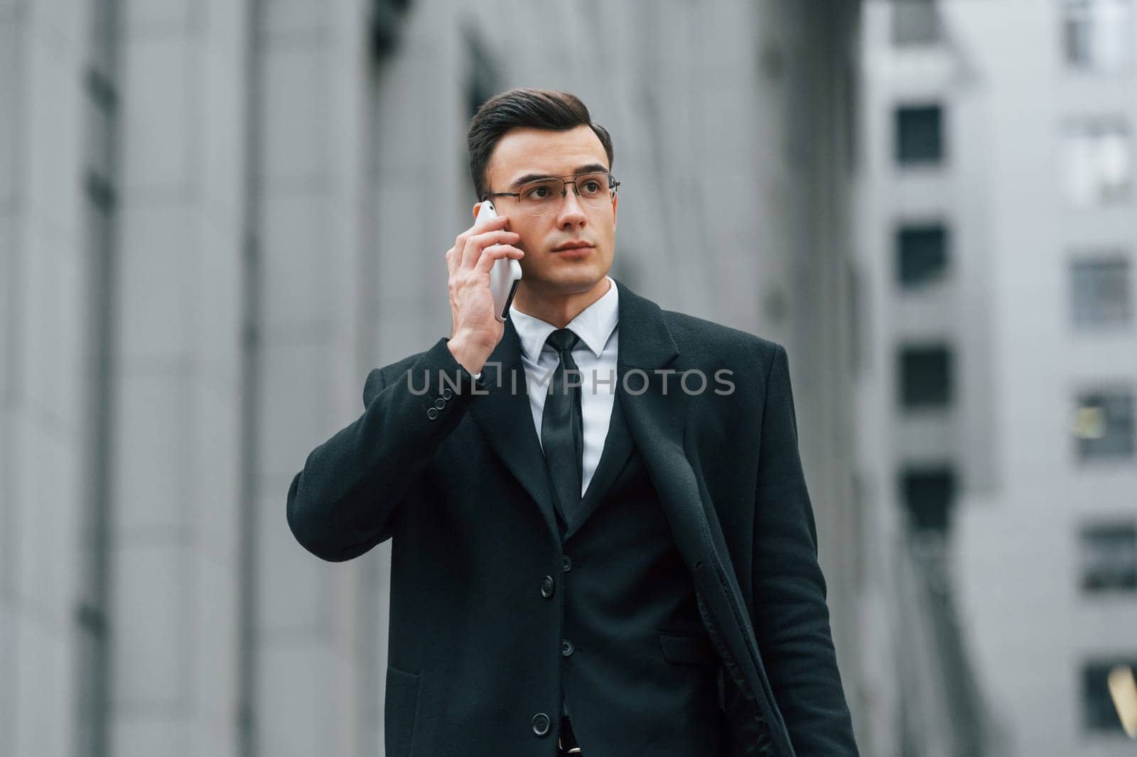 With smartphone. Businessman in black suit and tie is outdoors in the city.