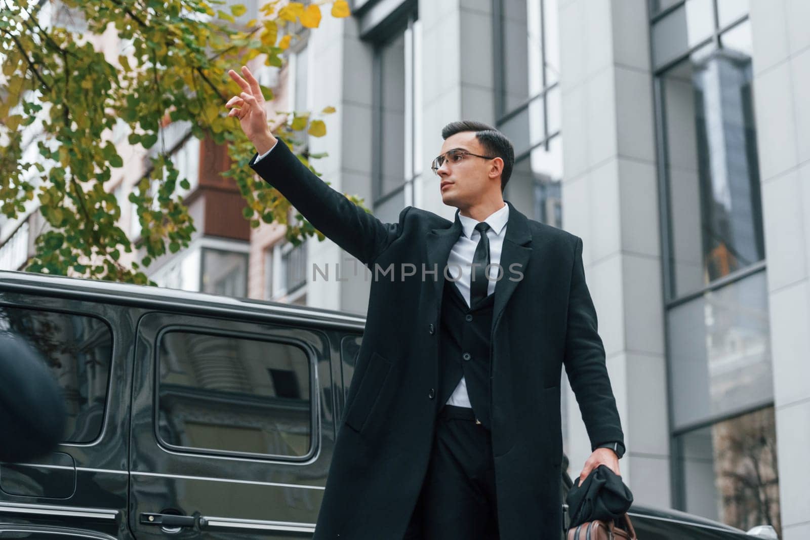 Calling taxi. Businessman in black suit and tie is outdoors in the city.