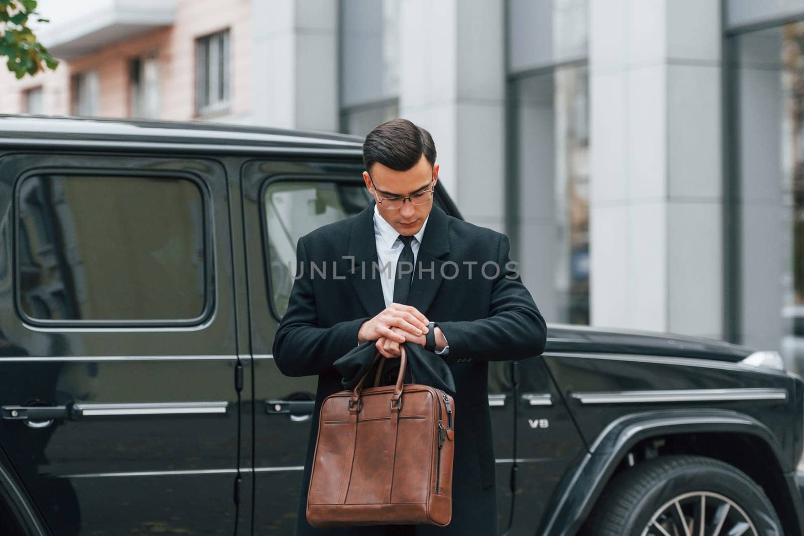 Holding brown bag in hands. Businessman in black suit and tie is outdoors in the city by Standret