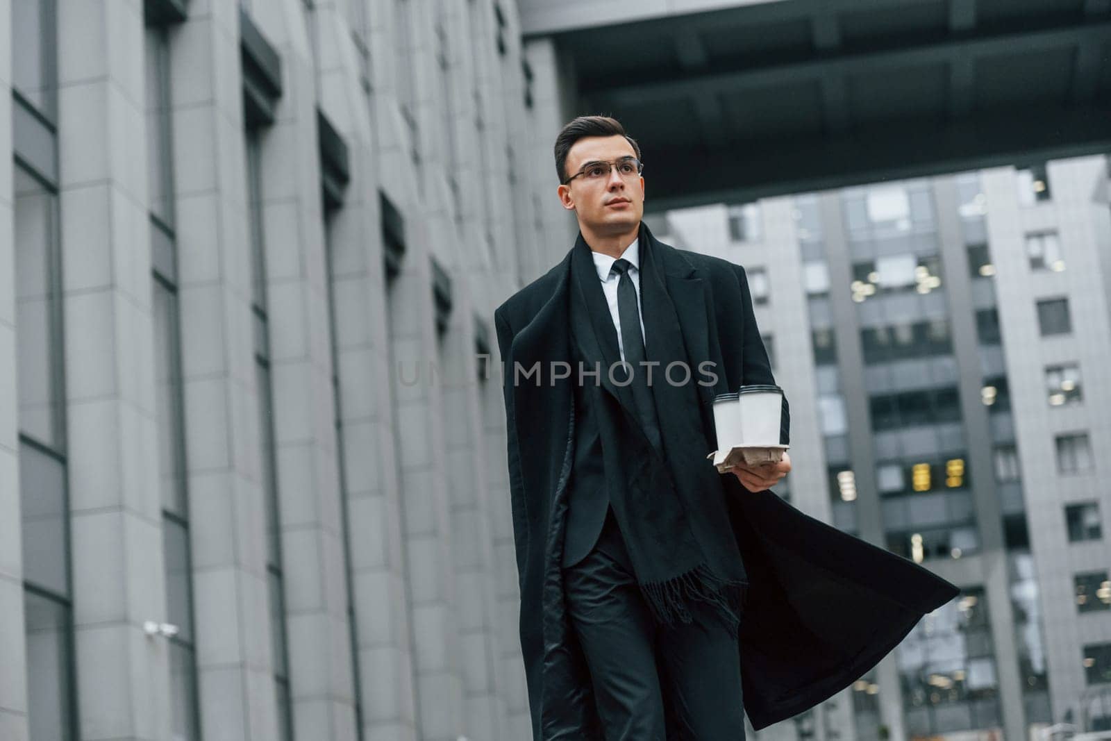 Walking forward. Businessman in black suit and tie is outdoors in the city.
