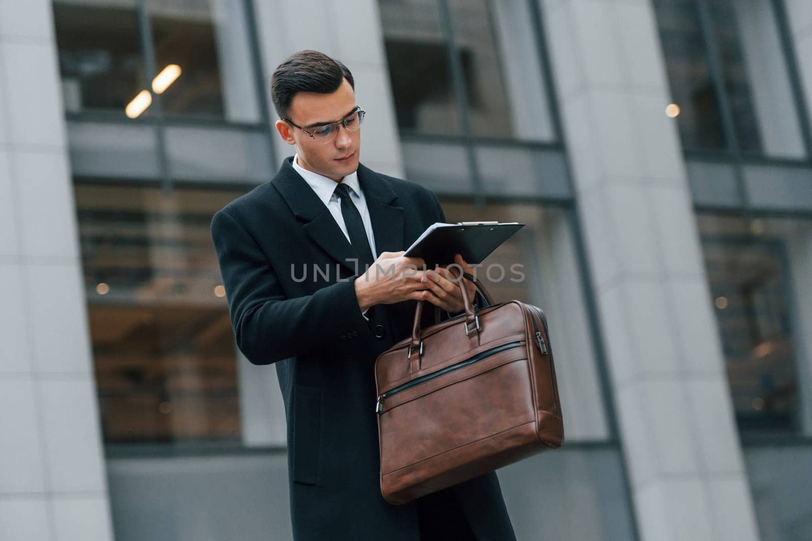 With brown bag. Businessman in black suit and tie is outdoors in the city.