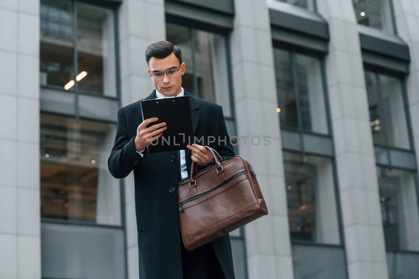 With brown bag. Businessman in black suit and tie is outdoors in the city by Standret