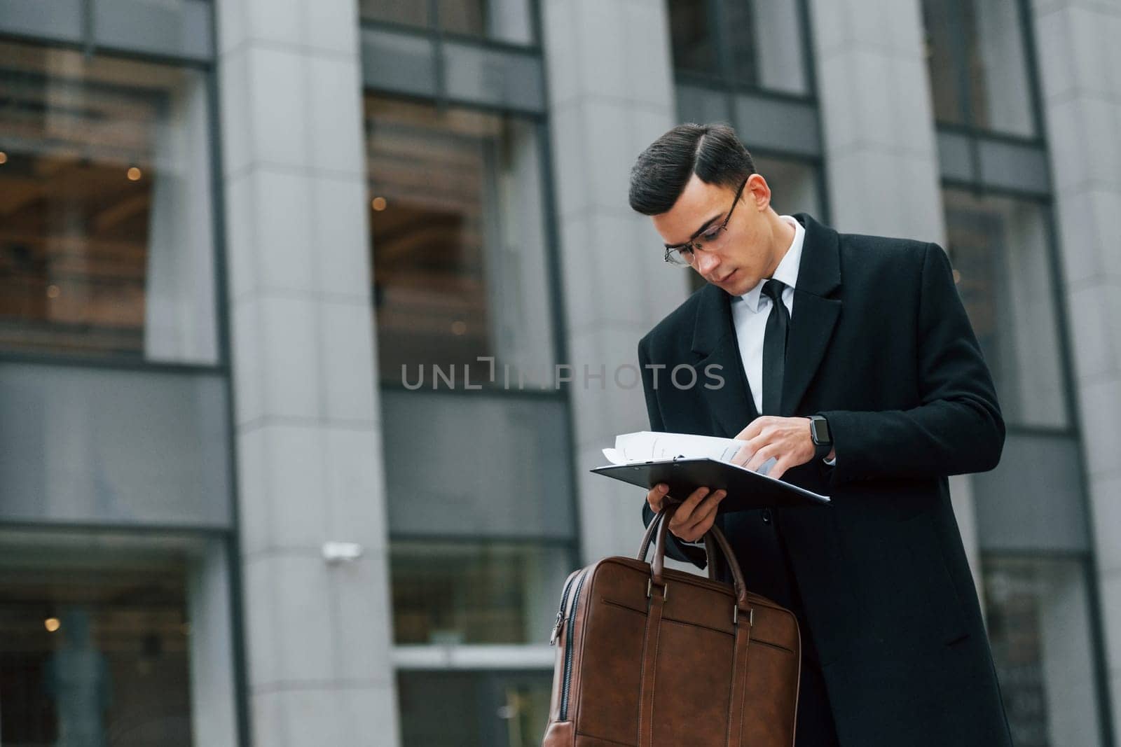 With brown bag. Businessman in black suit and tie is outdoors in the city.