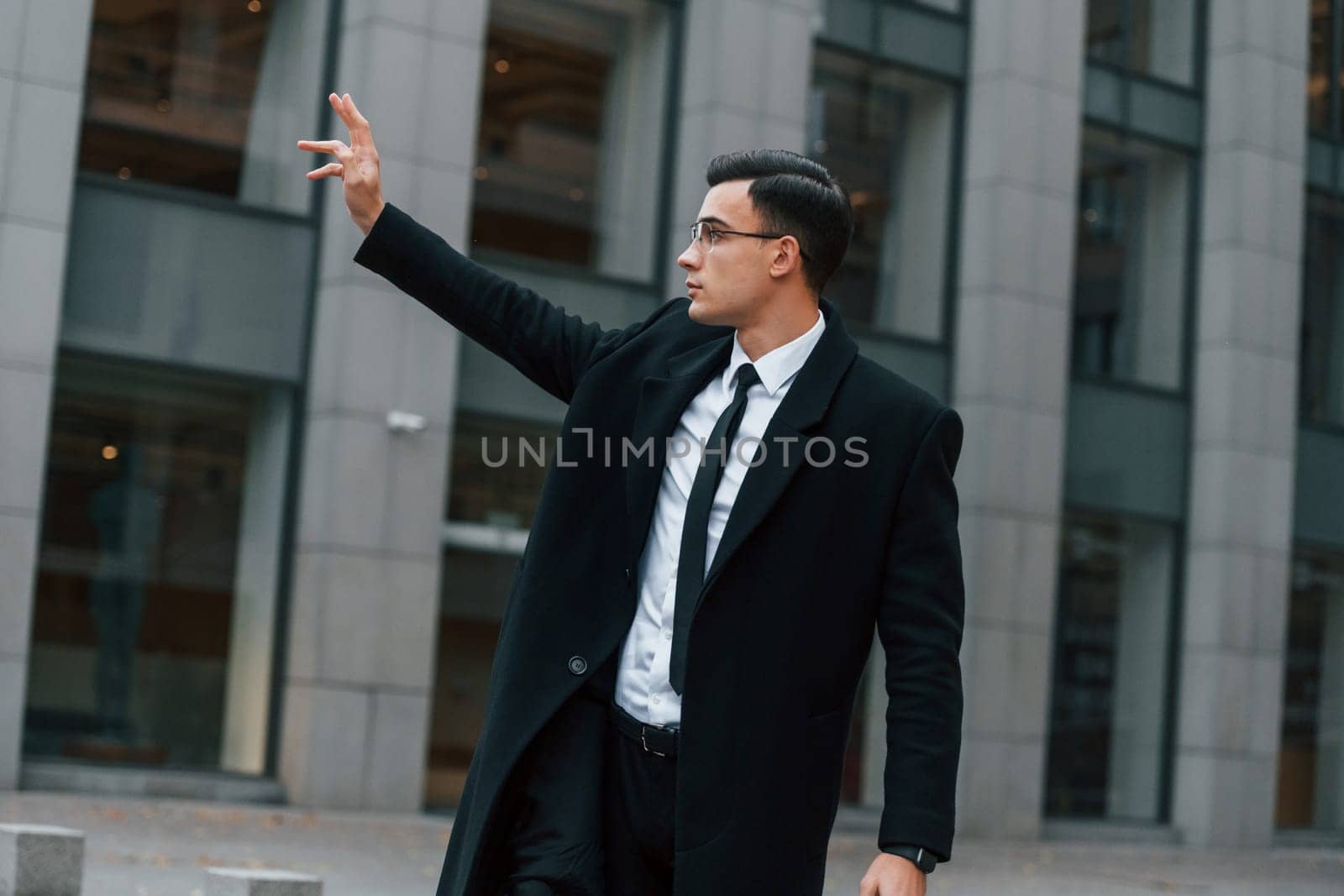 Calling for a taxi. Businessman in black suit and tie is outdoors in the city.