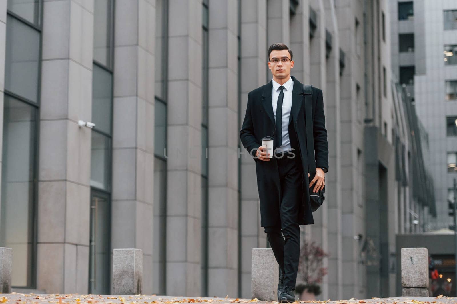 With cup of drink. Businessman in black suit and tie is outdoors in the city by Standret