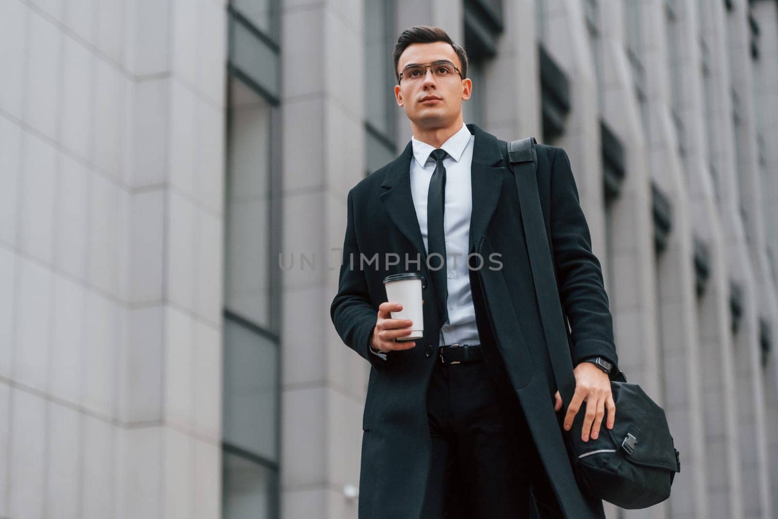 Front view. Businessman in black suit and tie is outdoors in the city.