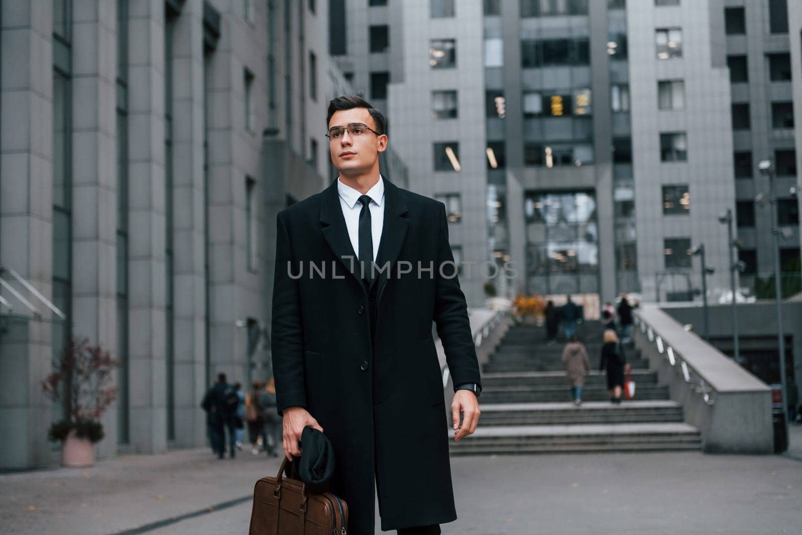 Front view. Businessman in black suit and tie is outdoors in the city.