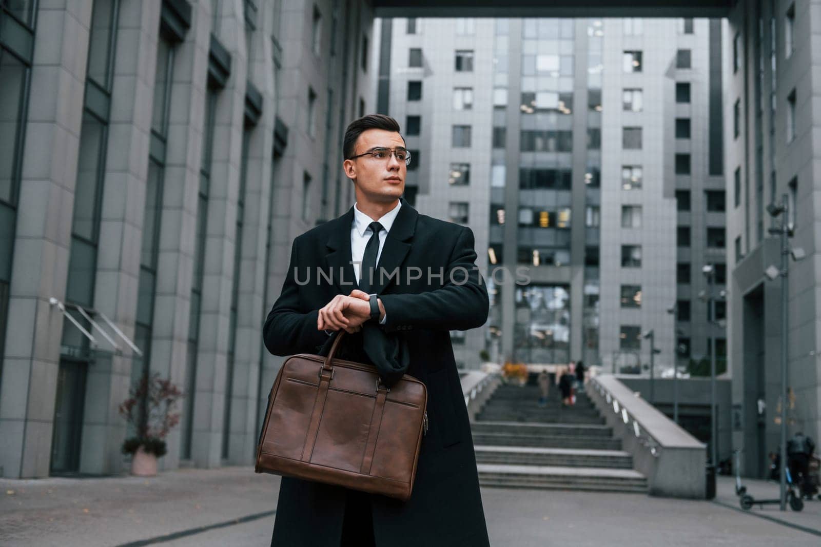 Front view. Businessman in black suit and tie is outdoors in the city by Standret