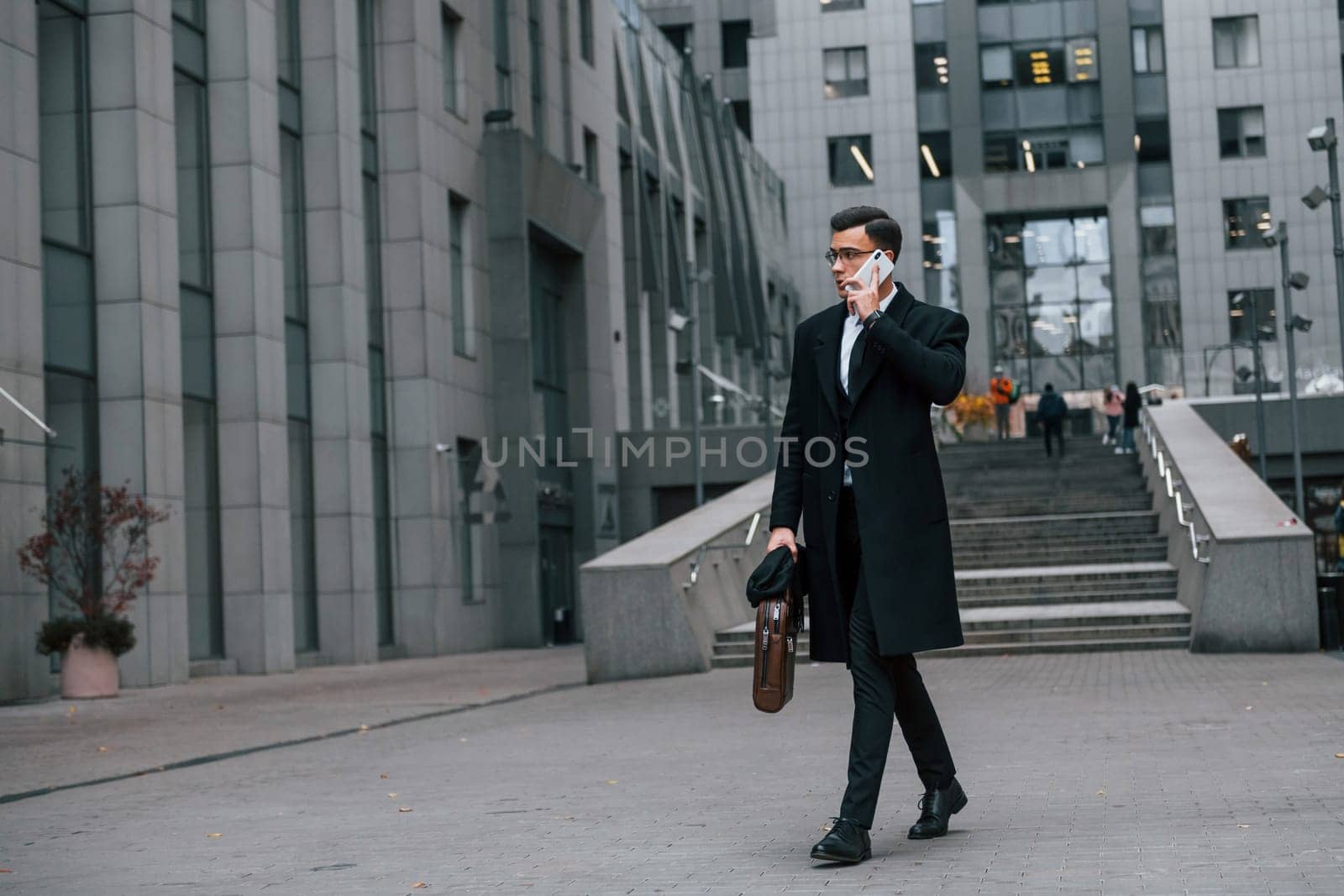 Phone in hand. Businessman in black suit and tie is outdoors in the city by Standret