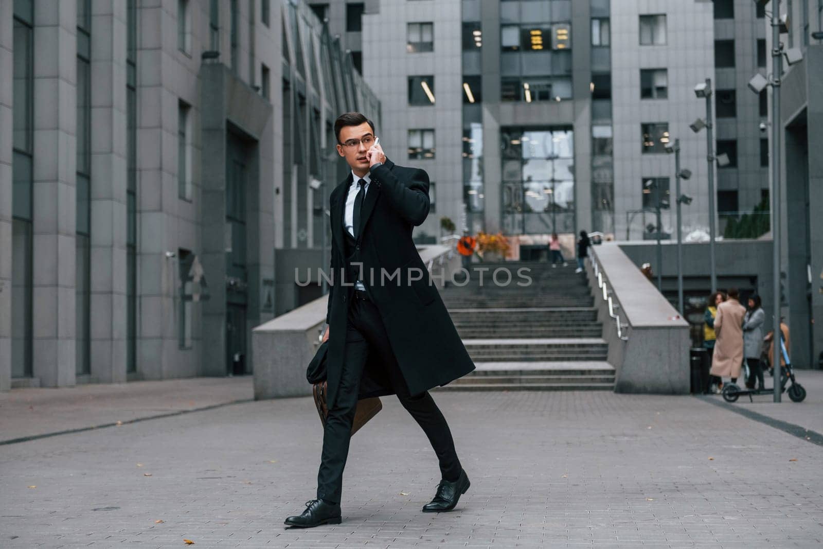 Phone in hand. Businessman in black suit and tie is outdoors in the city.
