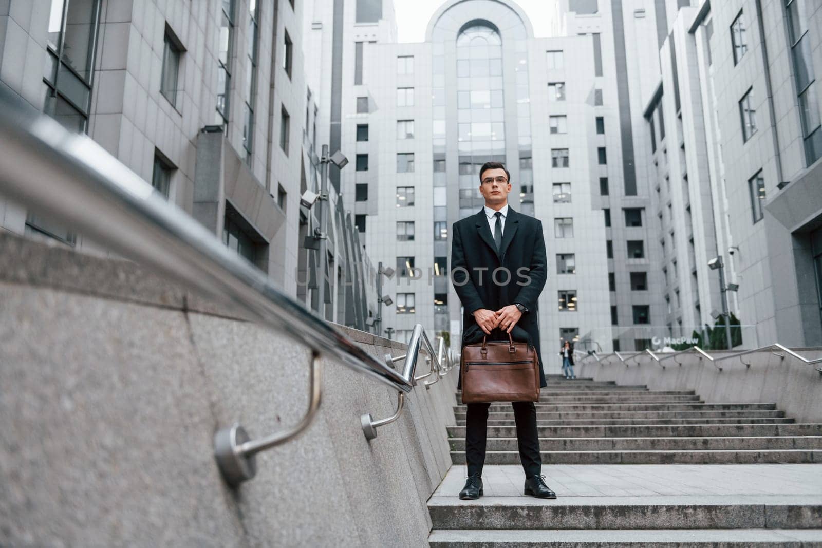 Buildings exterior. Businessman in black suit and tie is outdoors in the city by Standret