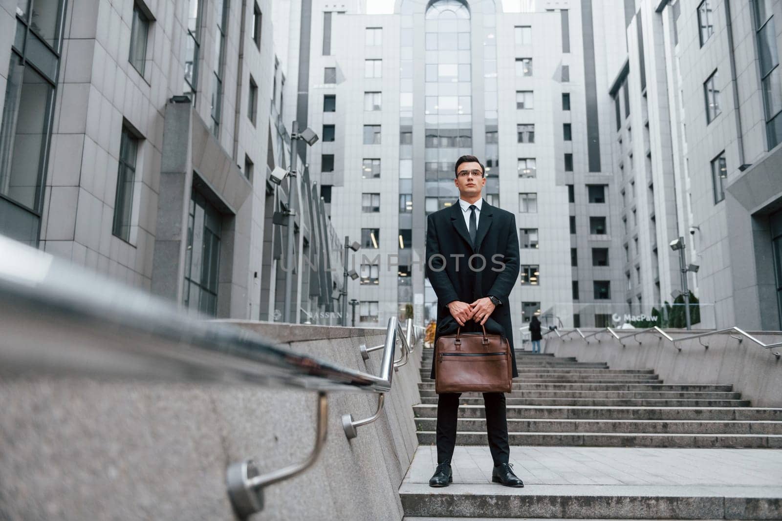 Buildings exterior. Businessman in black suit and tie is outdoors in the city by Standret