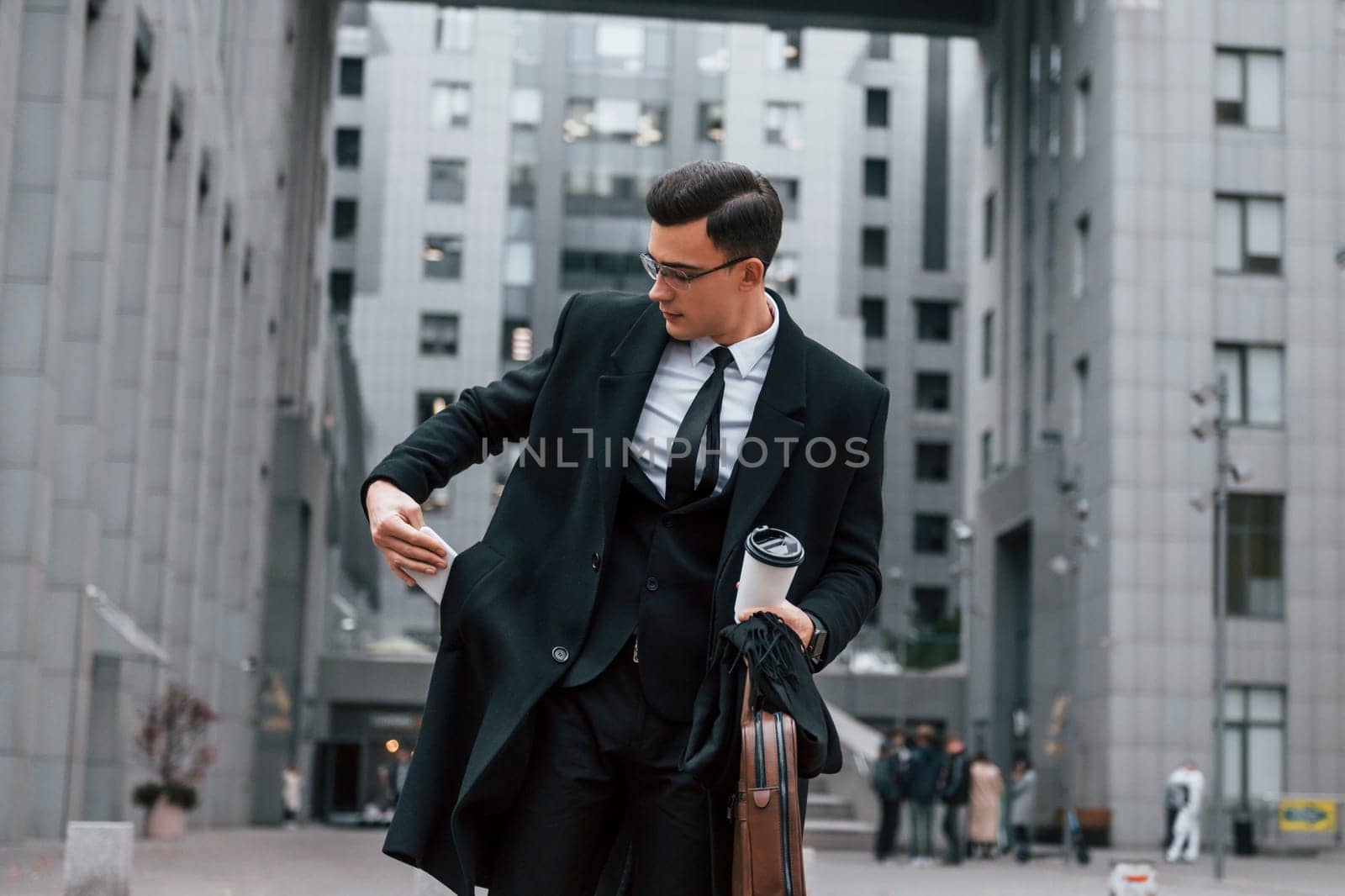 Buildings exterior. Businessman in black suit and tie is outdoors in the city.