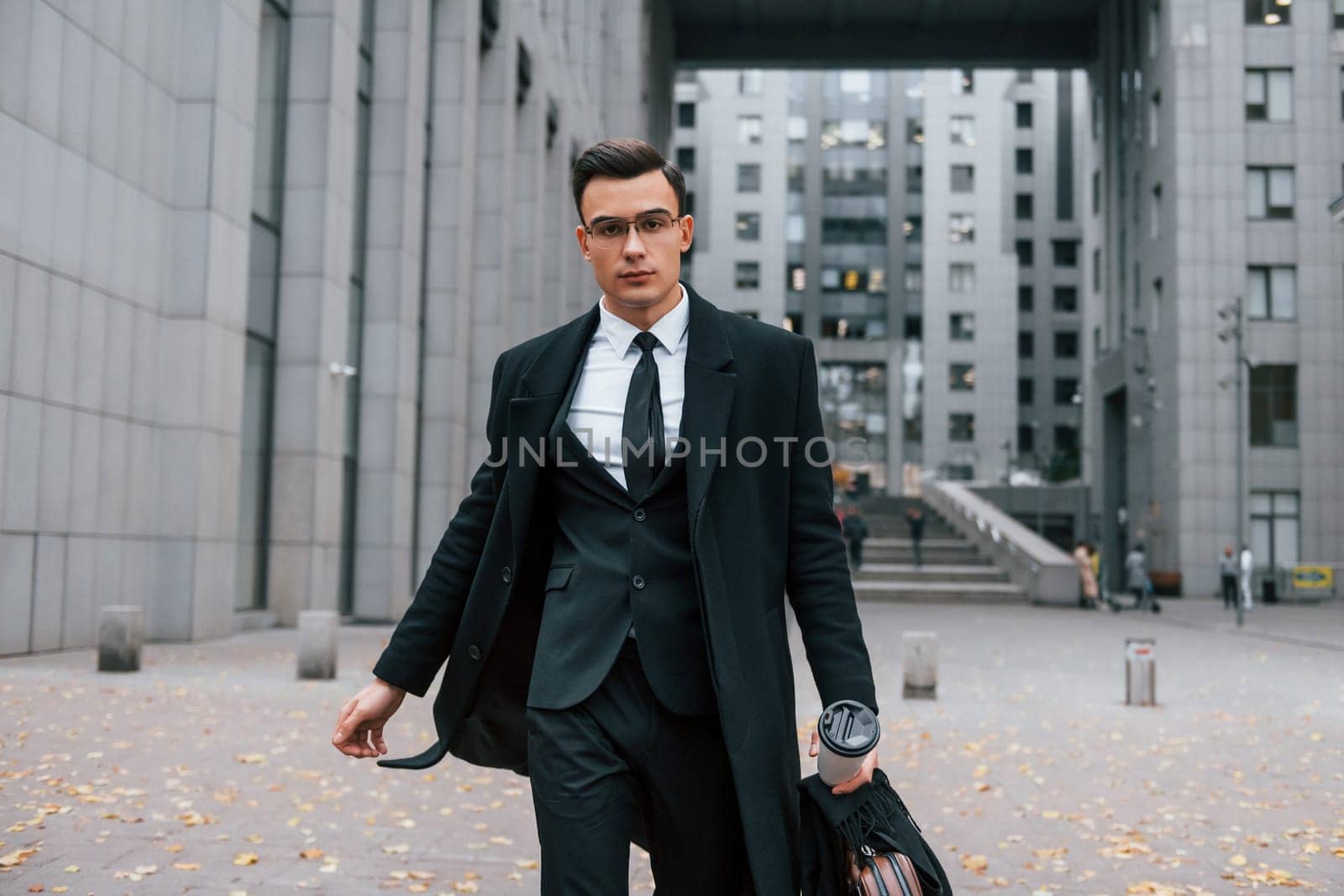 Walking forward. Businessman in black suit and tie is outdoors in the city.