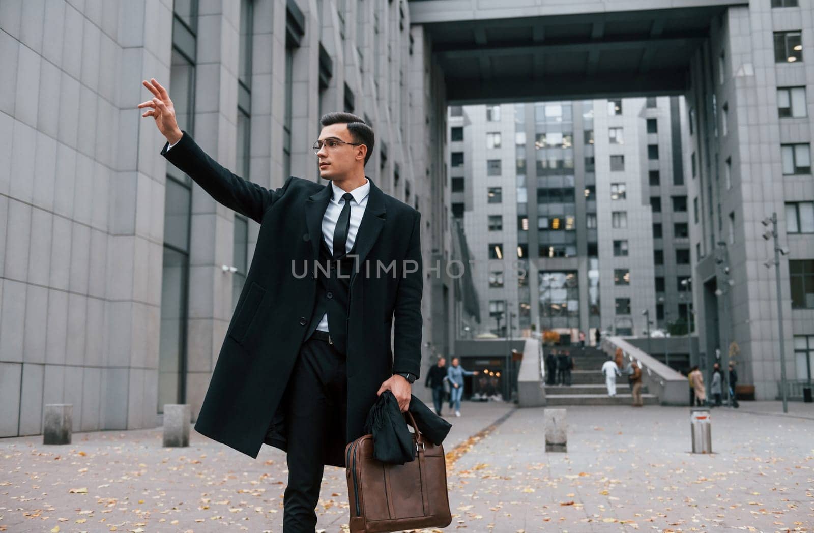 Looking for a taxi. Businessman in black suit and tie is outdoors in the city.