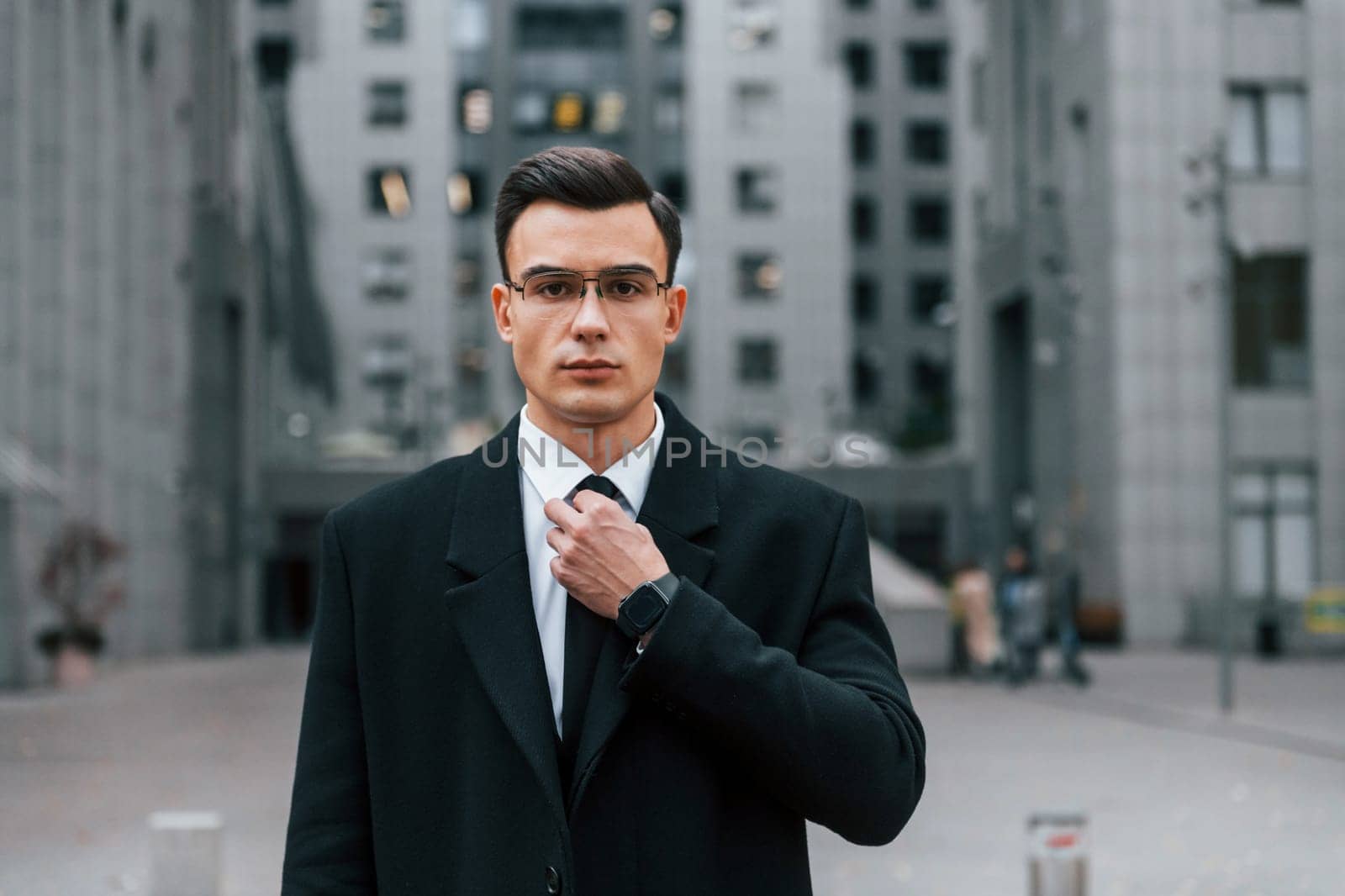 Fixing the tie. Businessman in black suit is outdoors in the city.