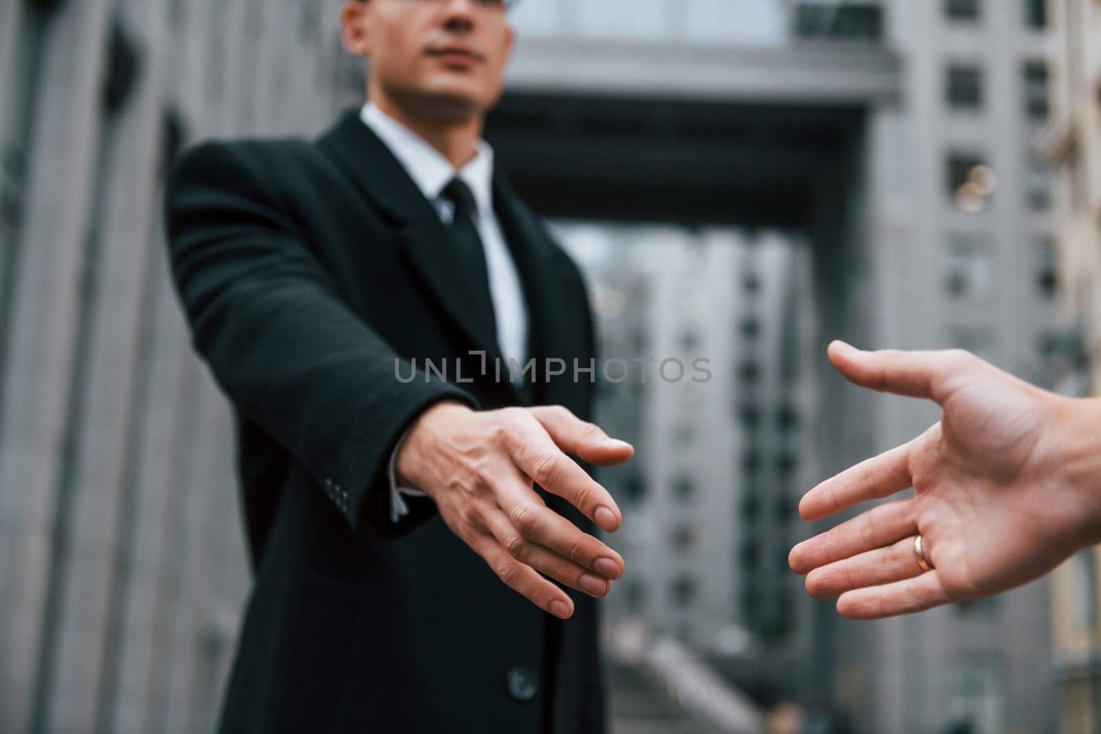 Doing handshake. Businessman in black suit and tie is outdoors in the city by Standret