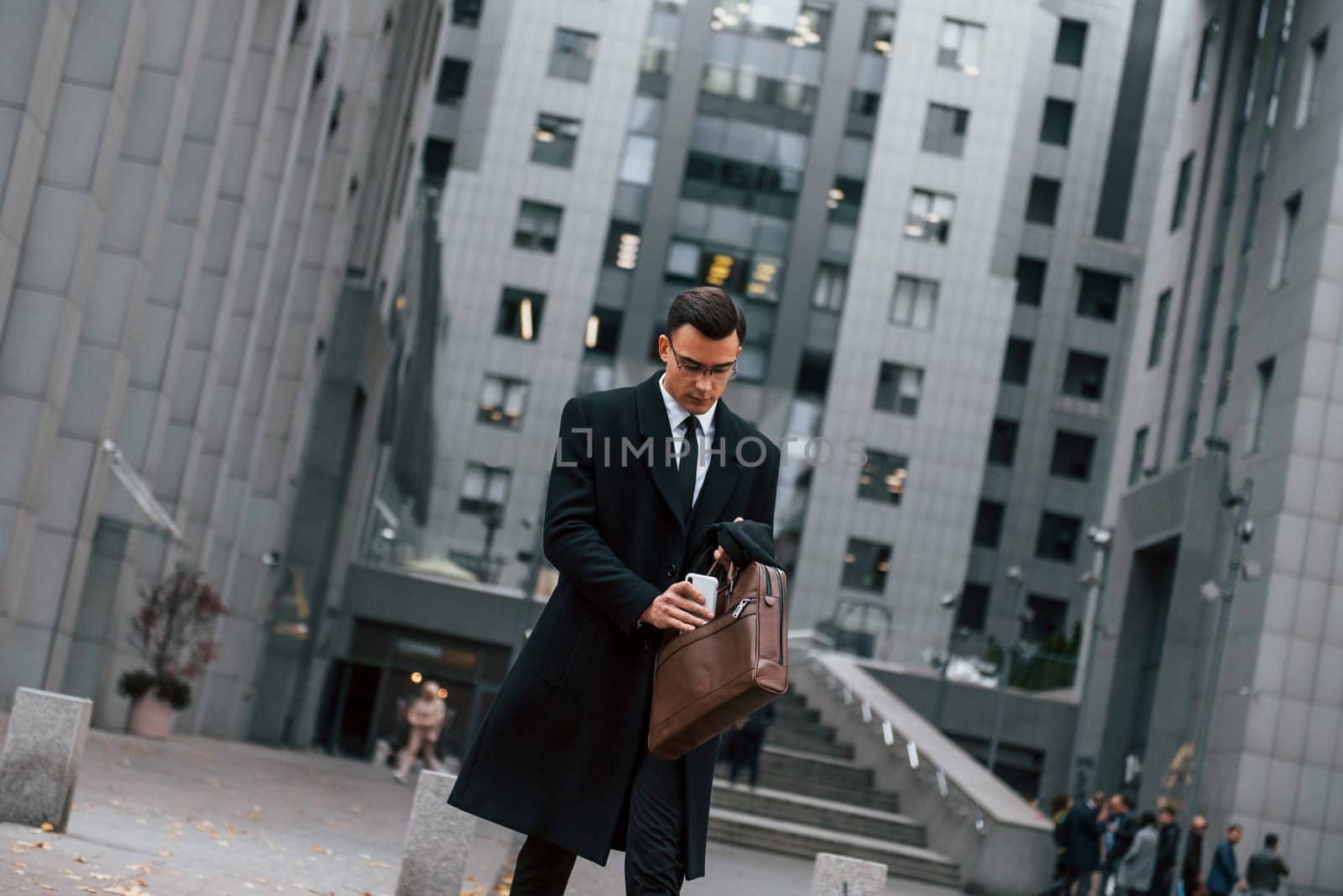 In formal clothes. Businessman in black suit and tie is outdoors in the city.