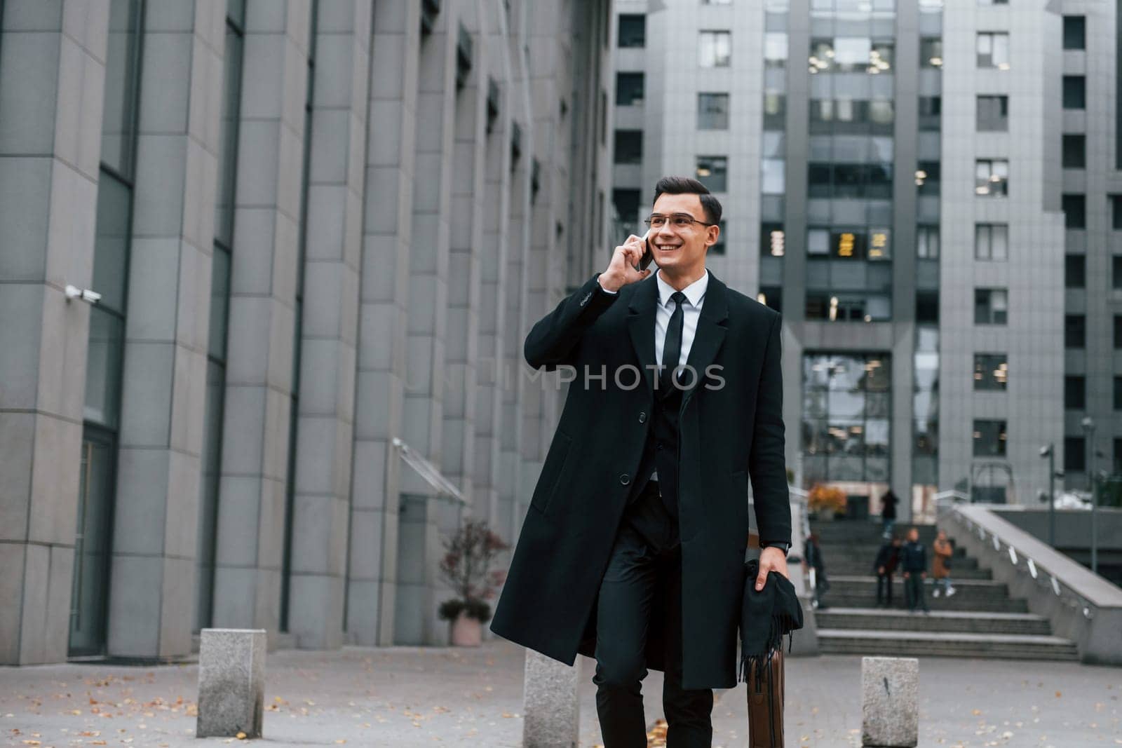 In formal clothes. Businessman in black suit and tie is outdoors in the city.