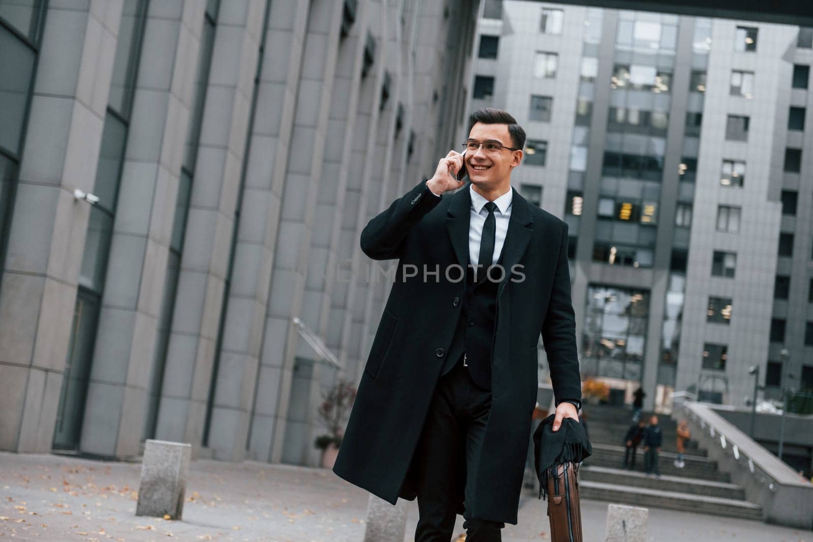 In formal clothes. Businessman in black suit and tie is outdoors in the city.