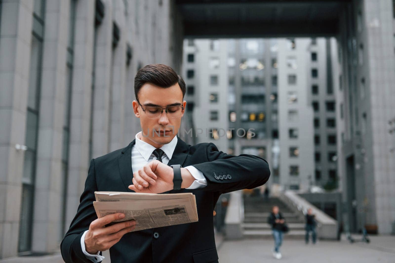 Reading some news. Businessman in black suit and tie is outdoors in the city.