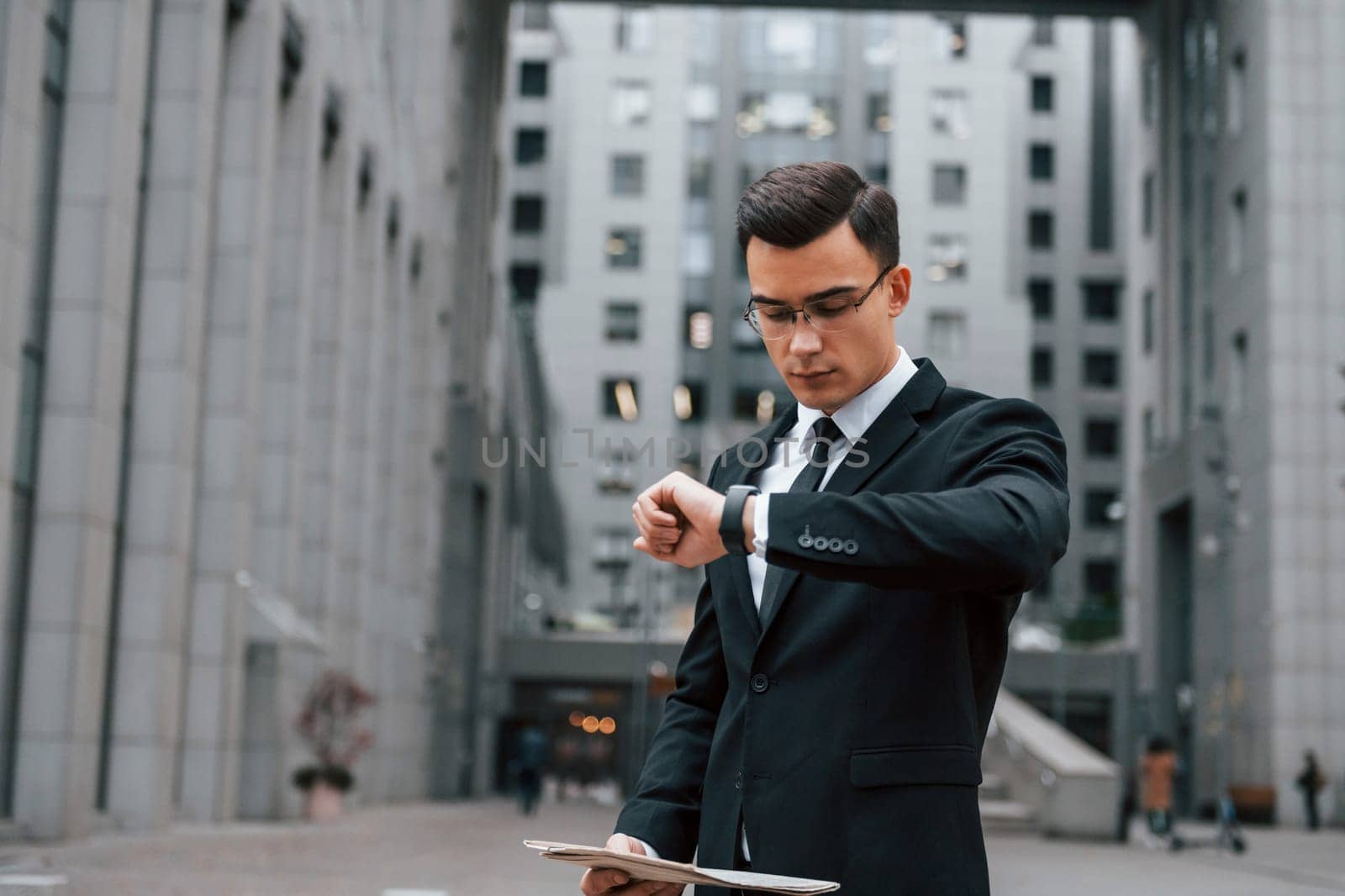 Reading some news. Businessman in black suit and tie is outdoors in the city by Standret