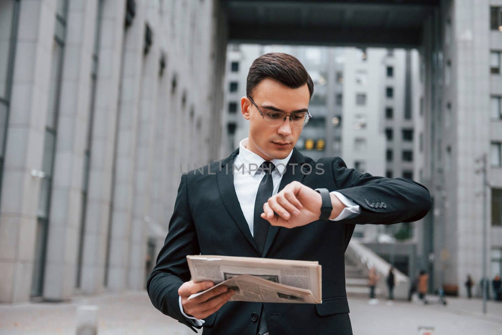 Checking the time. Businessman in black suit and tie is outdoors in the city.