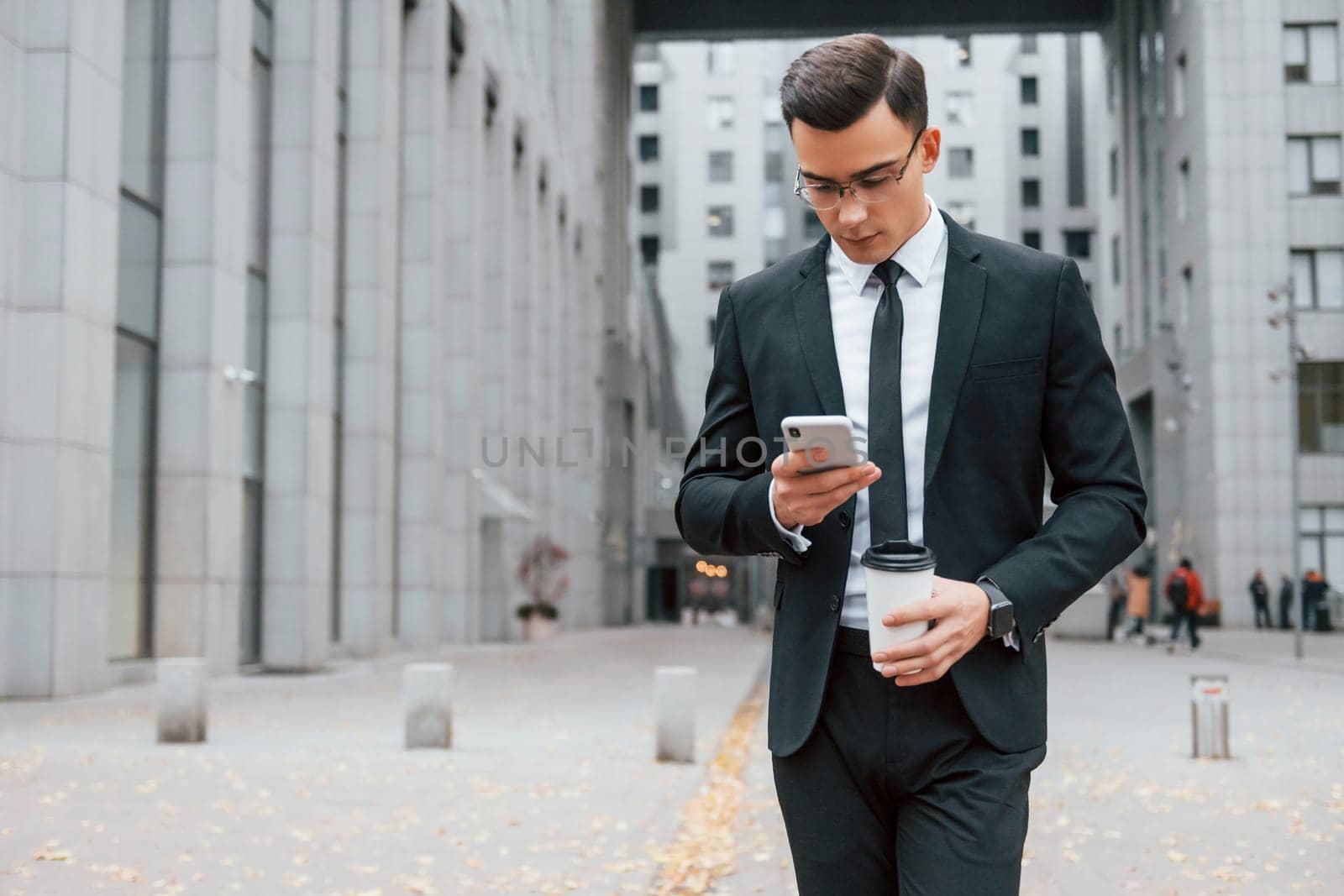 Internet communication by using smartphone. Businessman in black suit and tie is outdoors in the city.